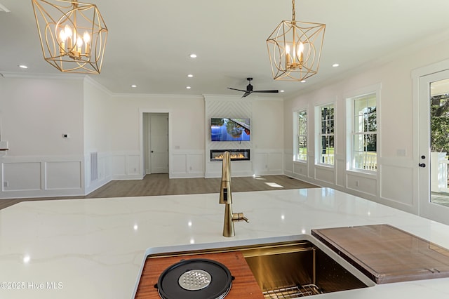 kitchen with ornamental molding, a decorative wall, a fireplace, open floor plan, and ceiling fan with notable chandelier