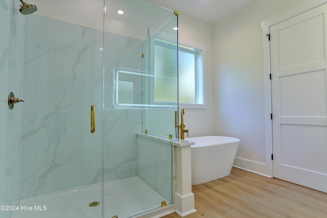 full bath featuring a soaking tub, wood finished floors, baseboards, and a marble finish shower