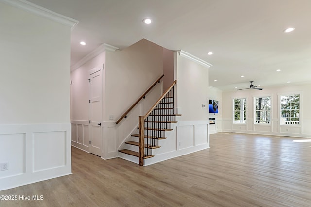 stairway featuring a ceiling fan, a decorative wall, ornamental molding, and wood finished floors