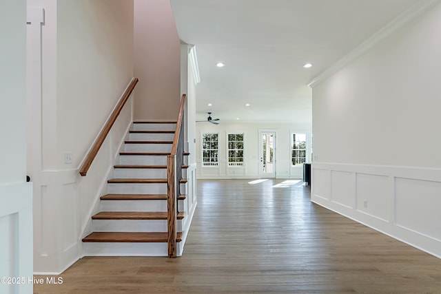 stairway featuring wood finished floors, recessed lighting, ornamental molding, and a decorative wall