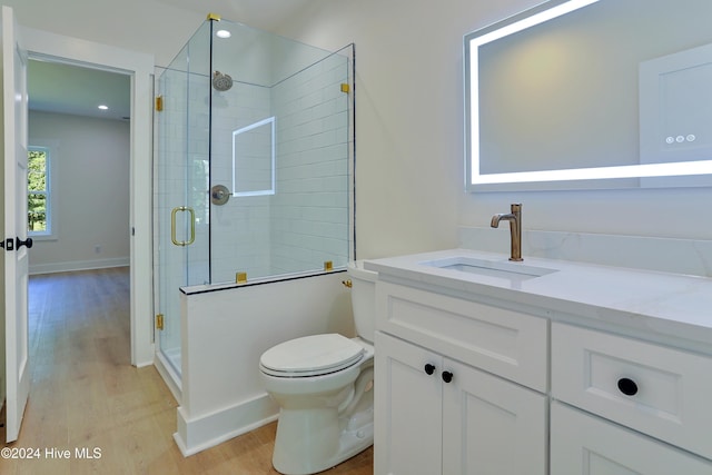 bathroom featuring toilet, wood finished floors, a stall shower, vanity, and baseboards