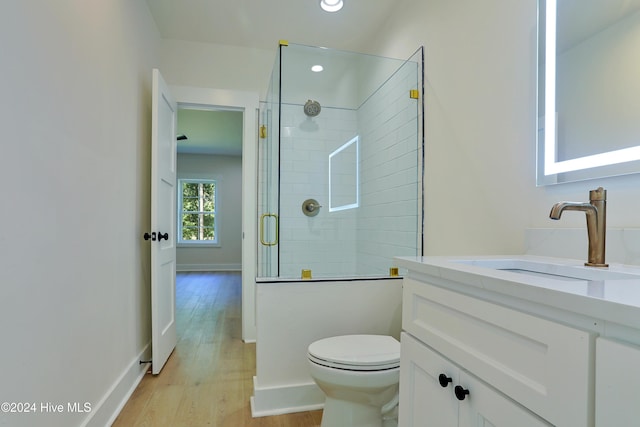bathroom with a tile shower, toilet, recessed lighting, wood finished floors, and vanity