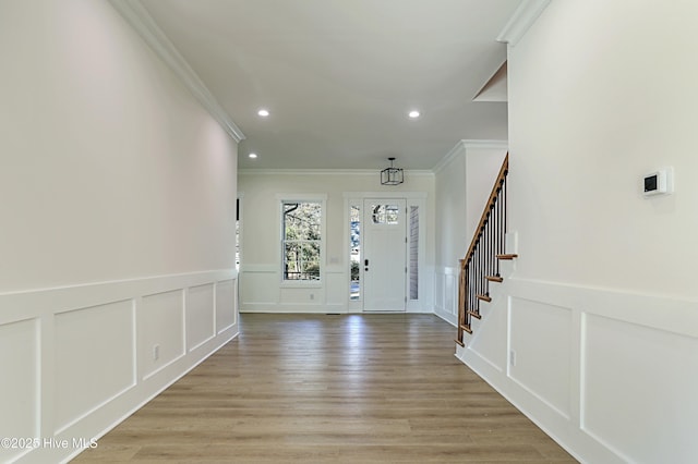 foyer entrance with a decorative wall, stairs, light wood-type flooring, ornamental molding, and recessed lighting