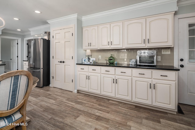 kitchen featuring decorative backsplash, stainless steel fridge, white cabinetry, hardwood / wood-style flooring, and ornamental molding