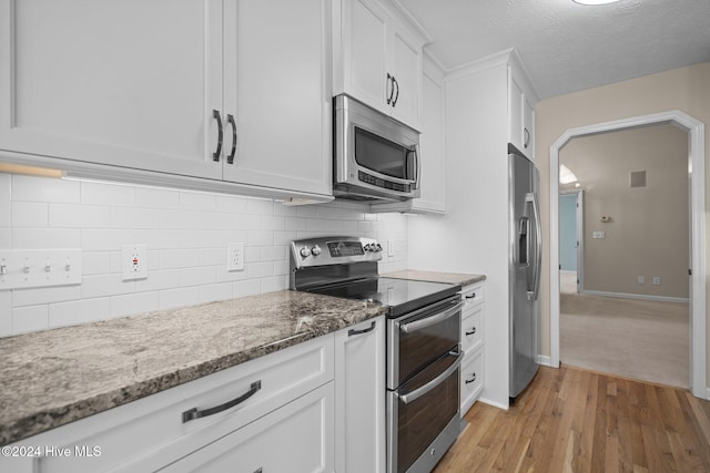 kitchen featuring tasteful backsplash, appliances with stainless steel finishes, light wood-type flooring, white cabinetry, and light stone counters