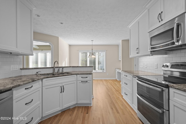 kitchen featuring sink, light wood-type flooring, hanging light fixtures, stainless steel appliances, and white cabinets