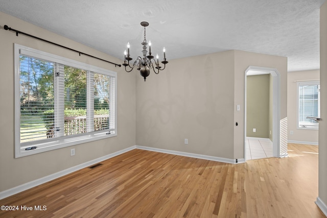 spare room featuring an inviting chandelier, a textured ceiling, and light wood-type flooring