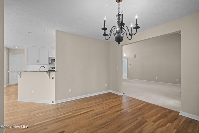 empty room featuring light hardwood / wood-style floors, a notable chandelier, and a textured ceiling