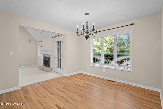 spare room featuring a notable chandelier, a textured ceiling, lofted ceiling, and light wood-type flooring