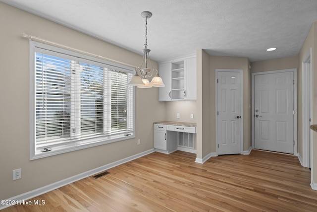 unfurnished dining area featuring a chandelier, a textured ceiling, and light wood-type flooring