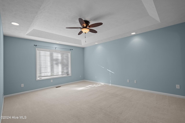 empty room with a textured ceiling, ceiling fan, light colored carpet, and a raised ceiling