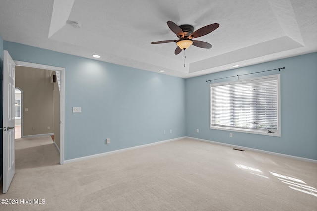 carpeted empty room with a textured ceiling, a tray ceiling, and ceiling fan