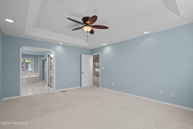 unfurnished bedroom featuring a raised ceiling, ceiling fan, light colored carpet, and ensuite bath