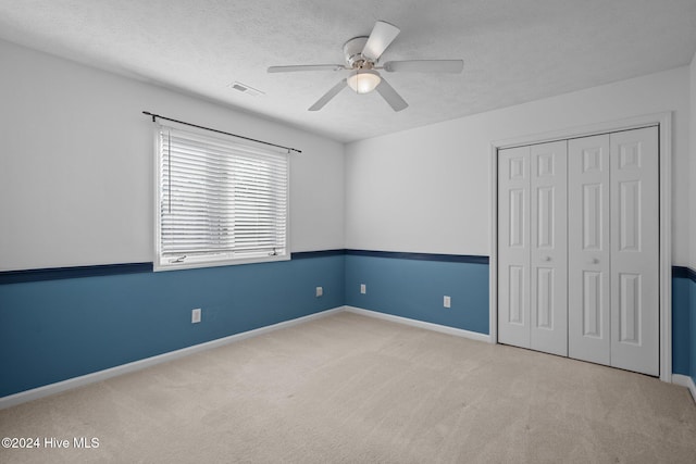 unfurnished bedroom featuring a closet, ceiling fan, light carpet, and a textured ceiling