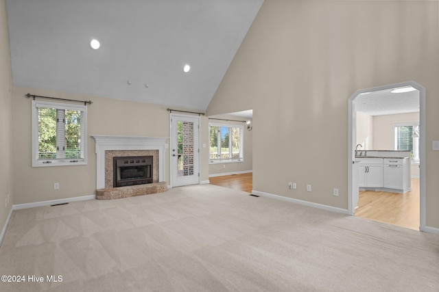 unfurnished living room featuring light carpet, high vaulted ceiling, and a wealth of natural light