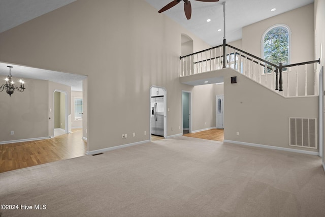 unfurnished living room with light hardwood / wood-style floors, high vaulted ceiling, and ceiling fan with notable chandelier