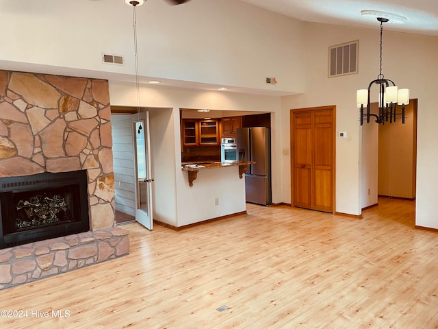 unfurnished living room featuring an inviting chandelier, light hardwood / wood-style floors, high vaulted ceiling, and a stone fireplace