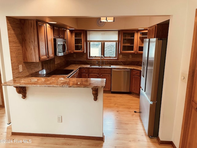 kitchen featuring kitchen peninsula, appliances with stainless steel finishes, a kitchen breakfast bar, tasteful backsplash, and sink