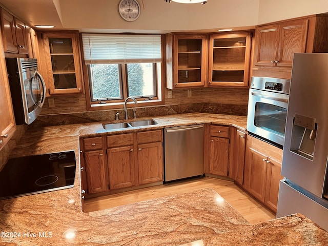 kitchen with light stone countertops, sink, stainless steel appliances, and light hardwood / wood-style flooring