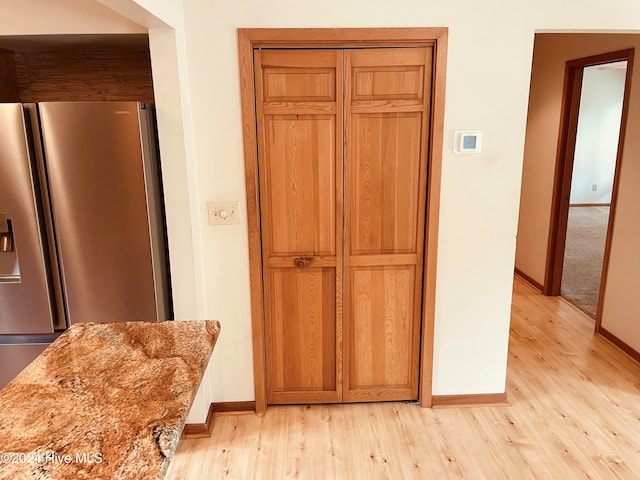 room details featuring light stone counters, light hardwood / wood-style flooring, and stainless steel refrigerator with ice dispenser