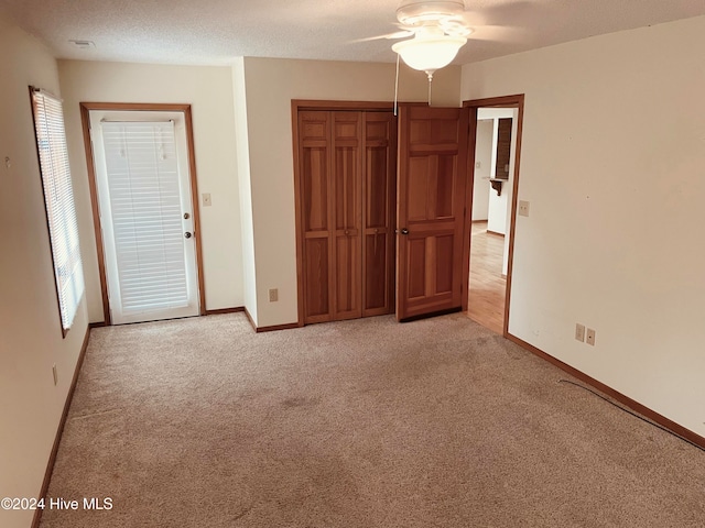 unfurnished bedroom featuring ceiling fan, light colored carpet, a textured ceiling, and a closet