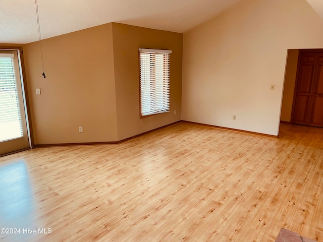 unfurnished room featuring light hardwood / wood-style floors, a textured ceiling, and vaulted ceiling