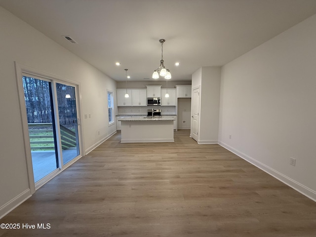 kitchen with light hardwood / wood-style floors, an island with sink, stainless steel appliances, decorative light fixtures, and white cabinets