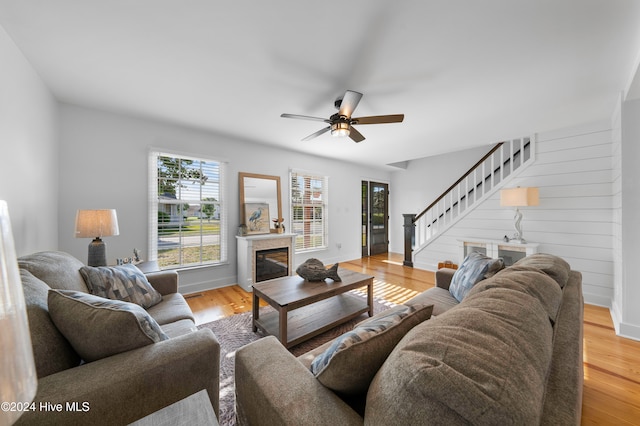 living room with ceiling fan, wooden walls, and light hardwood / wood-style floors