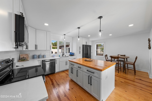 kitchen featuring appliances with stainless steel finishes, light wood-type flooring, pendant lighting, white cabinets, and a kitchen island