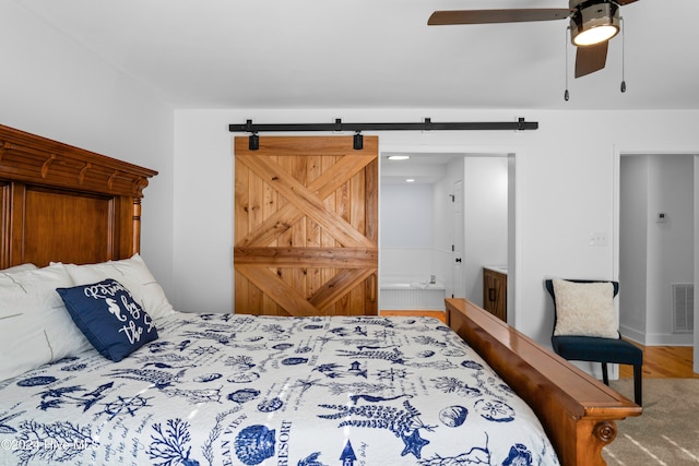 bedroom with connected bathroom, a barn door, ceiling fan, and carpet floors