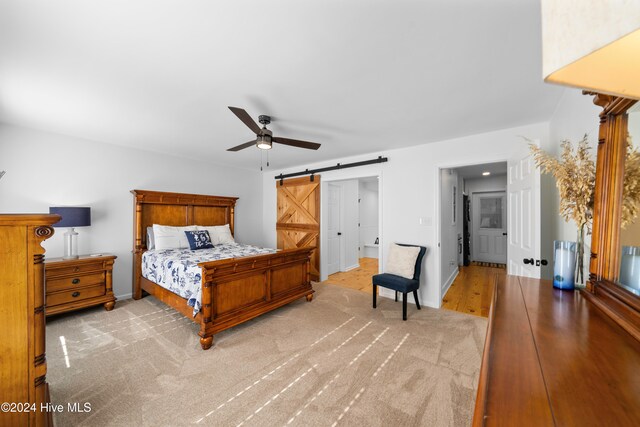 bedroom with a barn door, light hardwood / wood-style floors, and ceiling fan