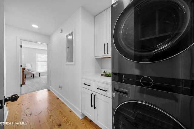 washroom with electric panel, cabinets, stacked washing maching and dryer, and light wood-type flooring