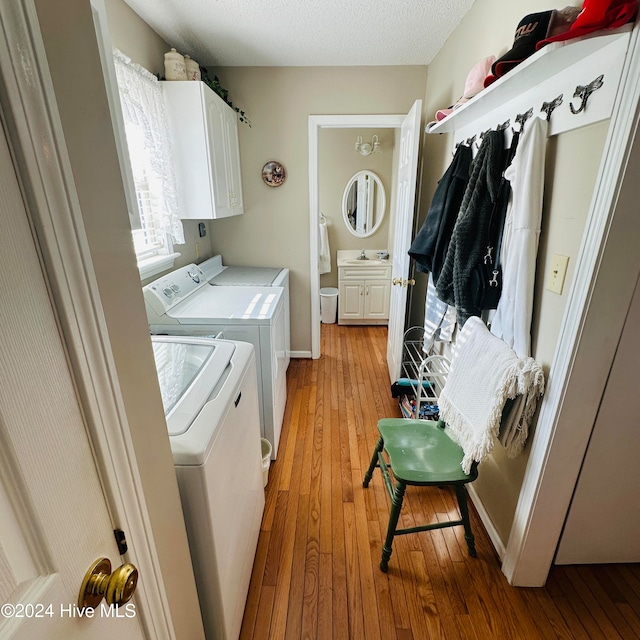 laundry area with sink, light wood-type flooring, a textured ceiling, washing machine and clothes dryer, and cabinets