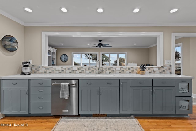 kitchen with stainless steel dishwasher, gray cabinetry, ornamental molding, a sink, and light wood-type flooring