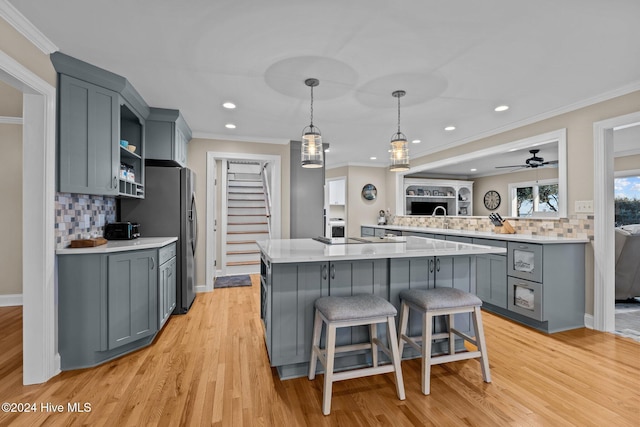 kitchen with a center island, light countertops, gray cabinetry, light wood-style floors, and a kitchen bar