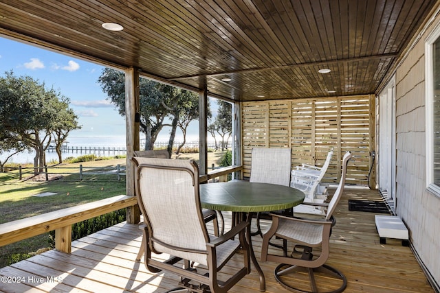 wooden terrace featuring outdoor dining space, a water view, and fence