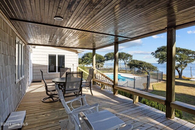 deck featuring outdoor dining space, a water view, fence, and a fenced in pool