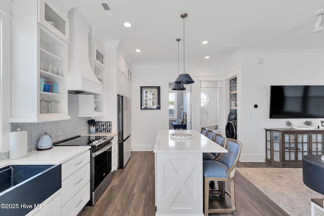 kitchen with a breakfast bar area, dark wood-style floors, premium range hood, stainless steel appliances, and glass insert cabinets