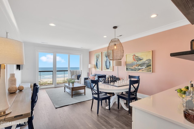 dining area featuring recessed lighting, wood finished floors, a water view, and ornamental molding