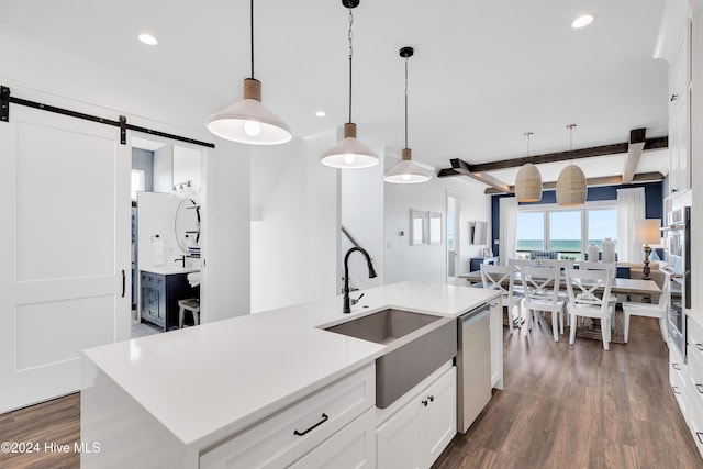 kitchen with beamed ceiling, a barn door, stainless steel dishwasher, dark wood-style floors, and a sink