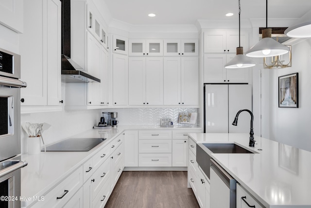 kitchen featuring black electric cooktop, a sink, freestanding refrigerator, wall chimney range hood, and dishwashing machine