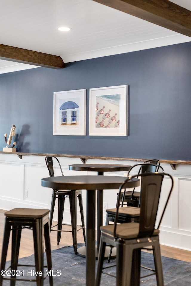 dining room with beam ceiling, wood finished floors, and a decorative wall