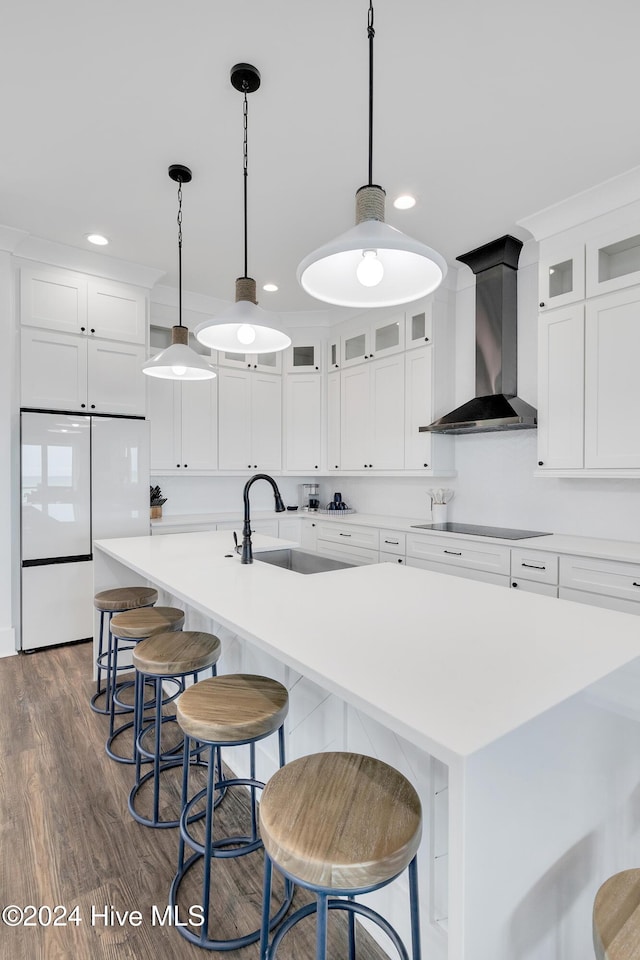 kitchen featuring a center island with sink, black electric stovetop, a sink, fridge, and wall chimney range hood