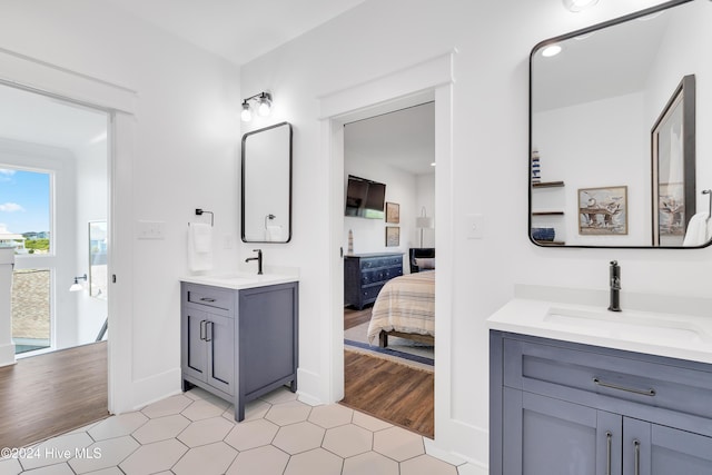 full bathroom with a sink, connected bathroom, two vanities, and wood finished floors