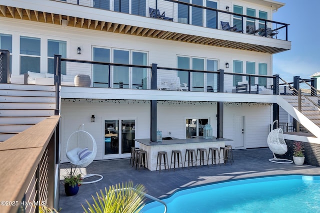 rear view of property with a balcony, a patio area, an outdoor pool, and outdoor dry bar