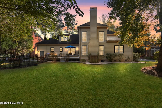 back house at dusk featuring a yard and a deck