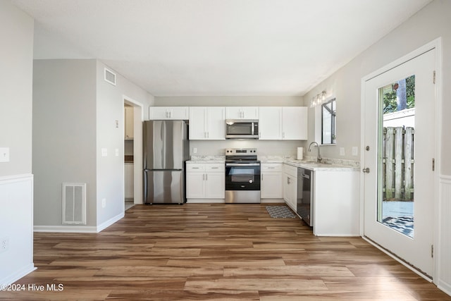 kitchen with light stone countertops, sink, white cabinetry, stainless steel appliances, and light hardwood / wood-style flooring