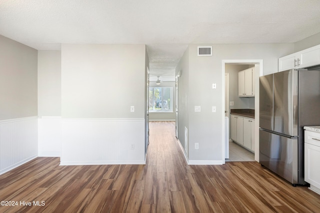 kitchen featuring white cabinetry, a textured ceiling, wood-type flooring, and stainless steel refrigerator