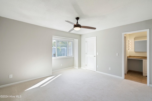 unfurnished bedroom featuring a textured ceiling, ensuite bathroom, light colored carpet, and ceiling fan