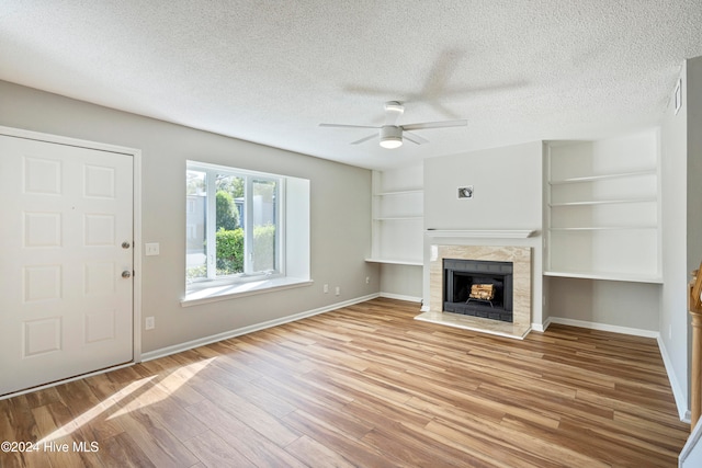 unfurnished living room with built in features, a textured ceiling, light wood-type flooring, and ceiling fan